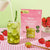 Blume Strawberry Matcha Superfood Powder pouch with an iced latte, spoon, and strawberries on a checkered tablecloth.